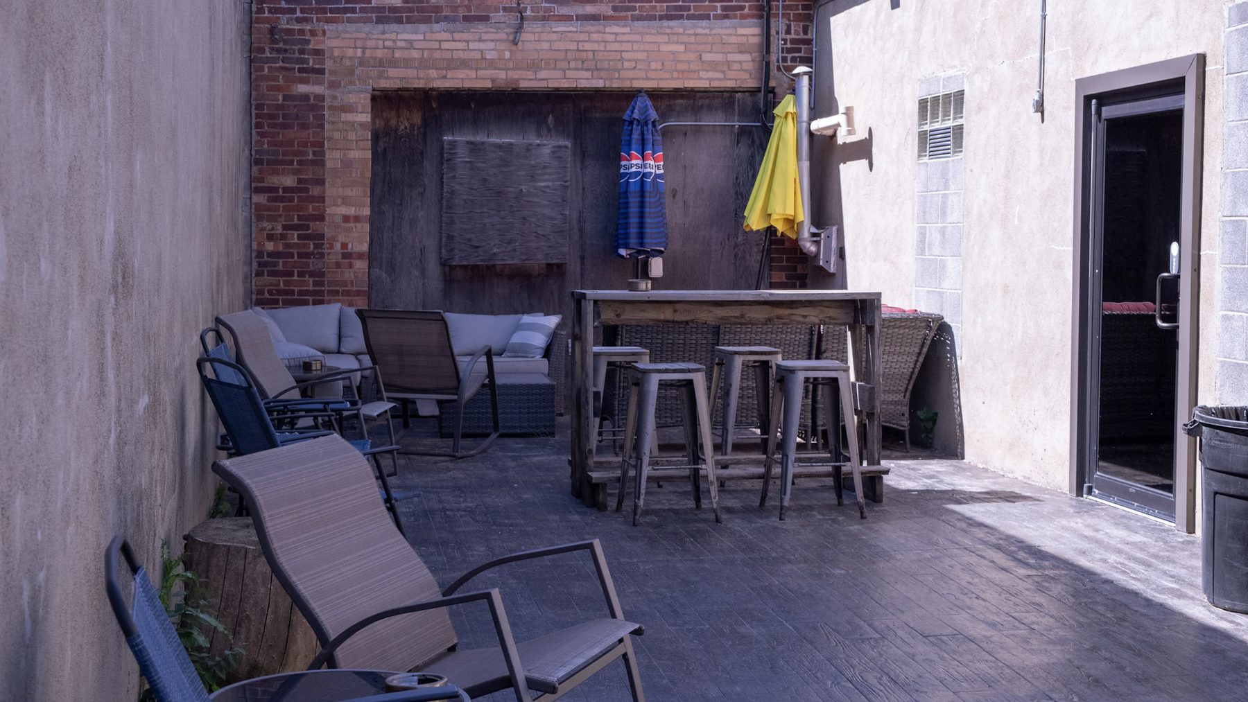 The outdoor patio at Burly's Roughrider, with high-top tables, umbrellas and patio seating against a brick wall